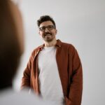 A cheerful man wearing glasses and a casual shirt standing indoors, captured naturally.